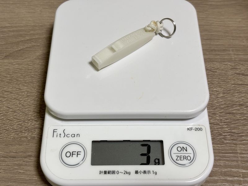 ストラップとキーリングを含めて3gのMIYAGEN 3D WHISTLE 2g with GLOW。計量器に載せて軽さを確認している様子。