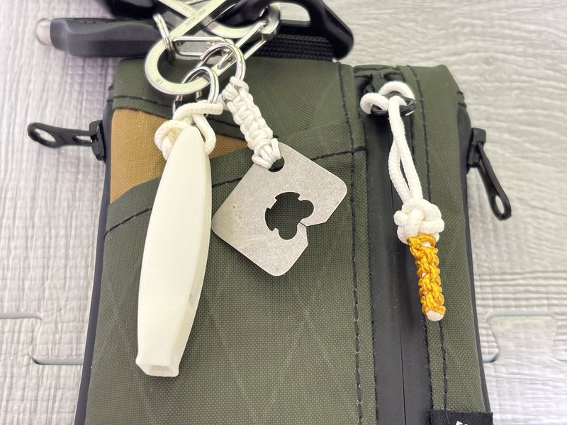EDCポーチに並ぶ白い蓄光ホイッスル、チタン製のパン留め、黄色い蓄光コードのジッパータブ